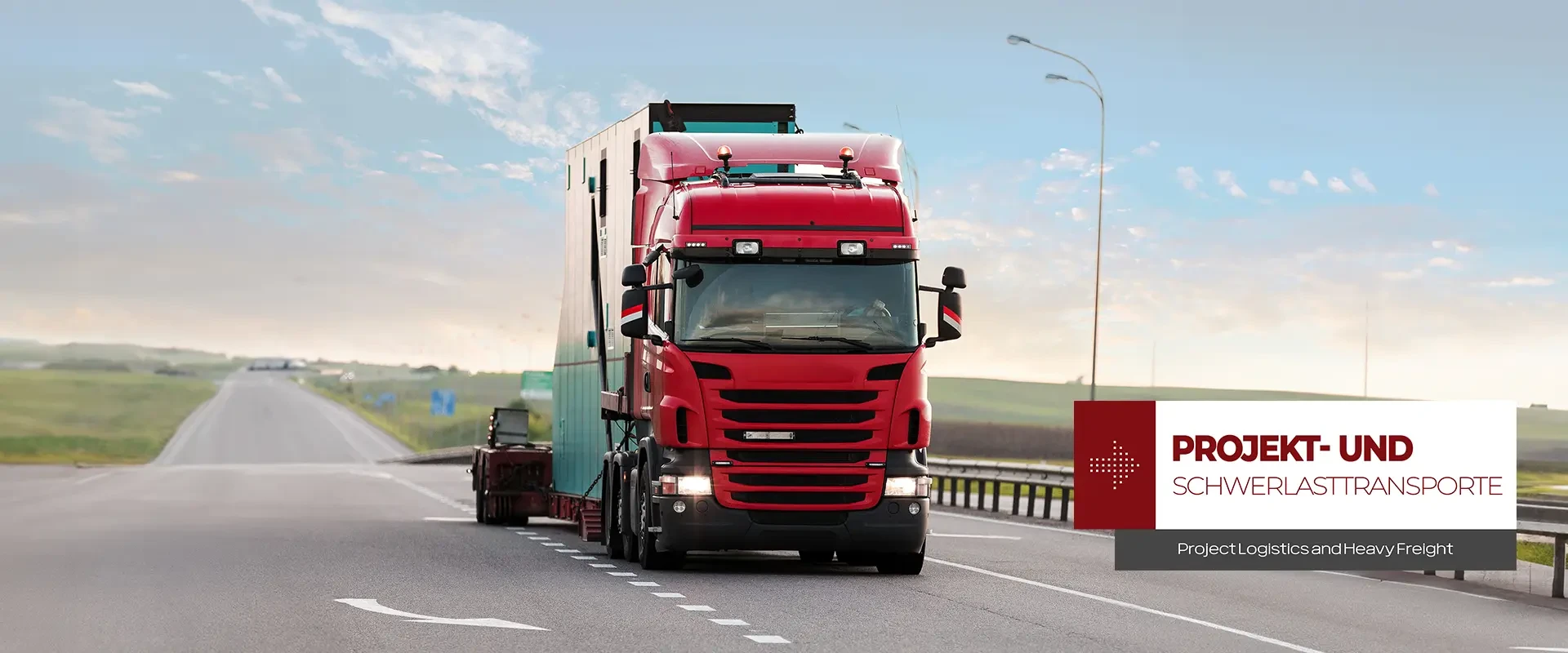 Ein roter Lastwagen fährt auf der Autobahn mit einem Tieflader, auf dem "Projekt- und Schwerlasttransport" steht