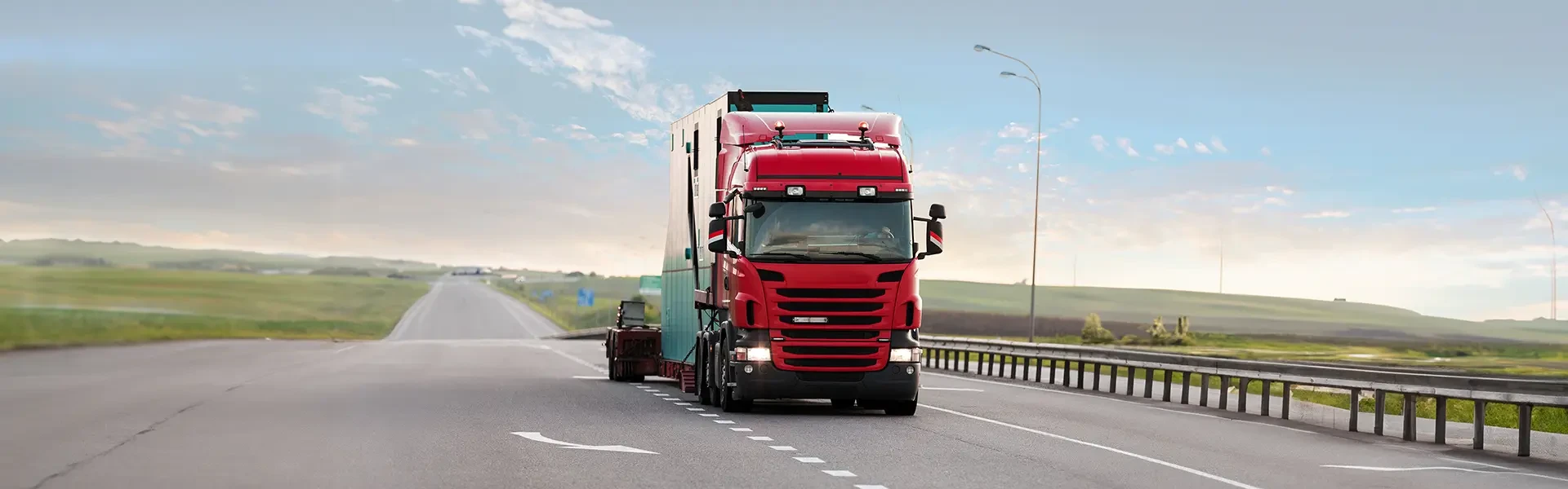 A red truck with a lowbed that says "Project and Heavy Load Transportation" on it is moving on the highway