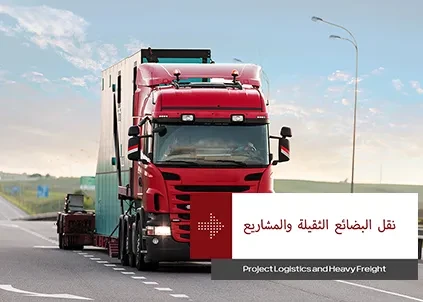 شاحنة حمراء تسير على الطريق السريع بشاحنة منخفضة تحمل علامة "المشروع ونقل الأحمال الثقيلة"